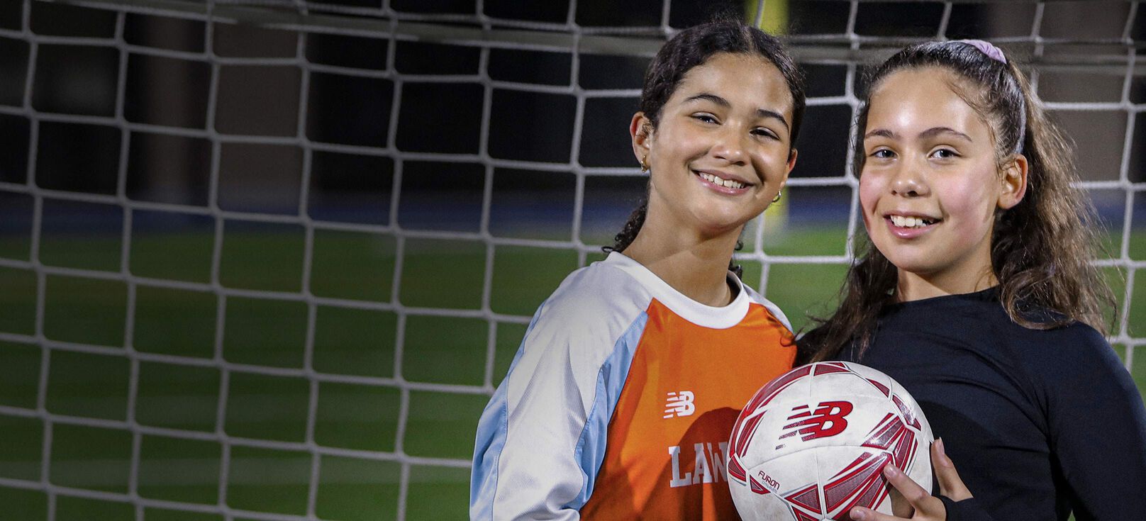 Two young female - presenting child holding football and smiling.